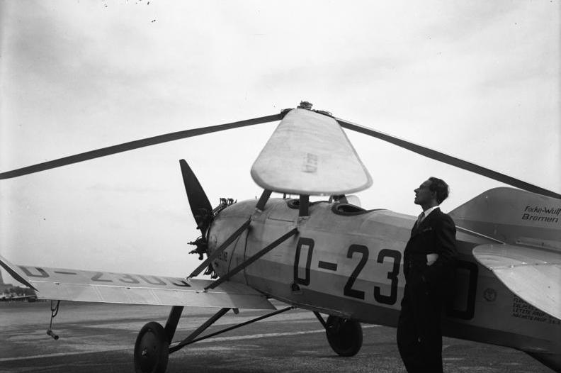 Vintage black and white photo of a man standing next to a small airplane on a runway.
