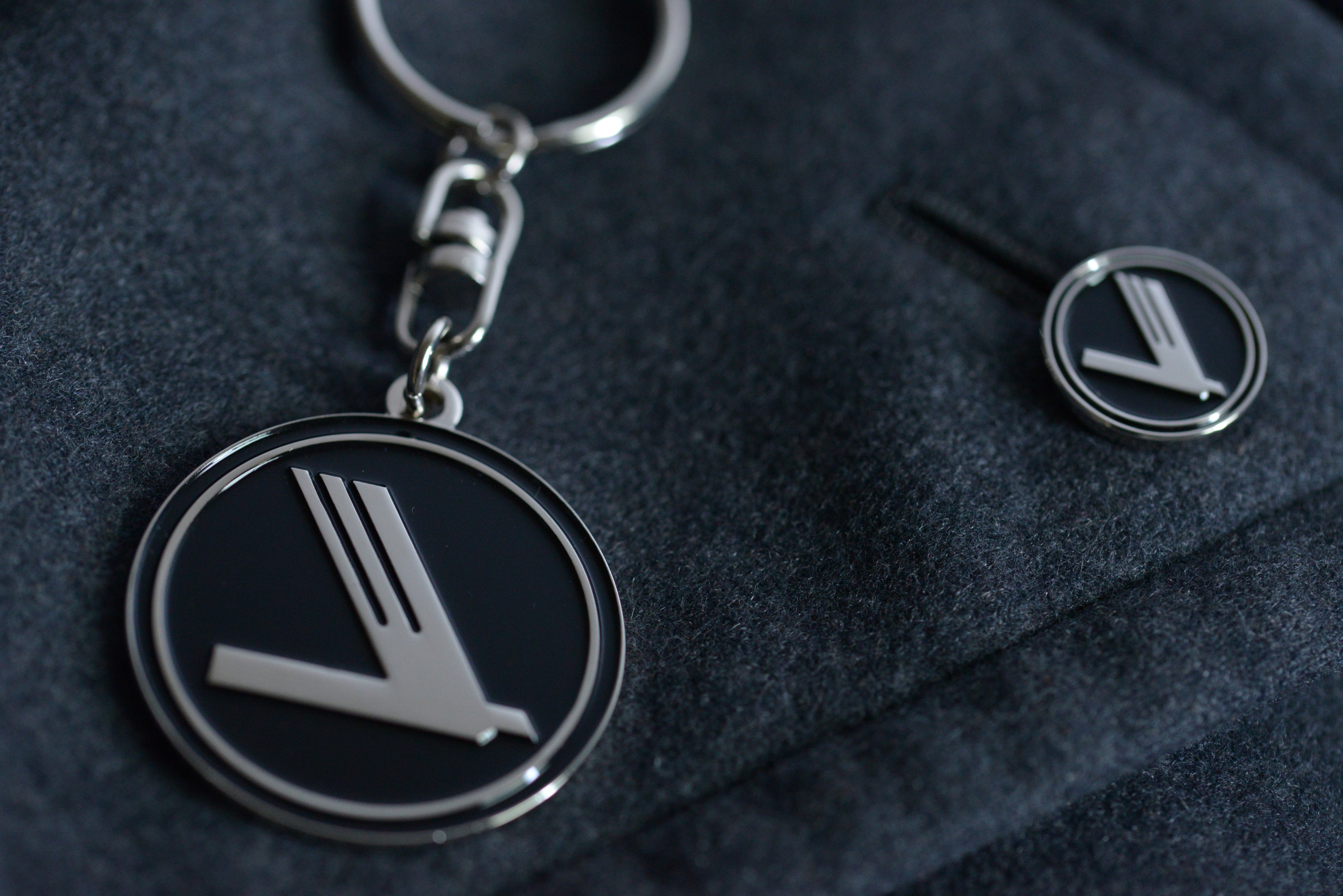 Keychain and lapel pin with a logo on a dark fabric background