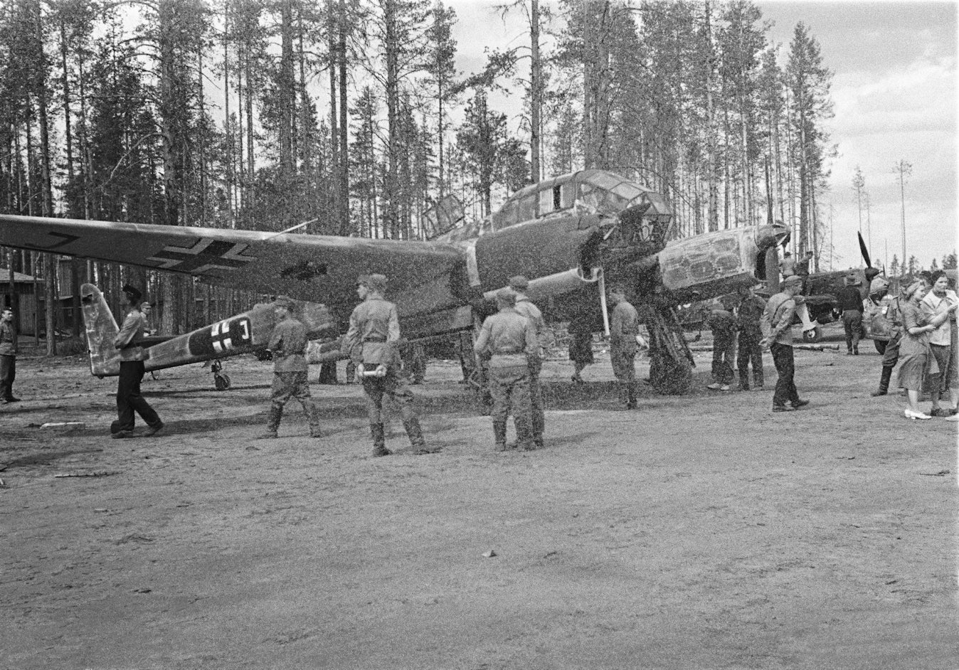 Vintage black and white photograph of military personnel around aircraft on a tarmac with trees in the background